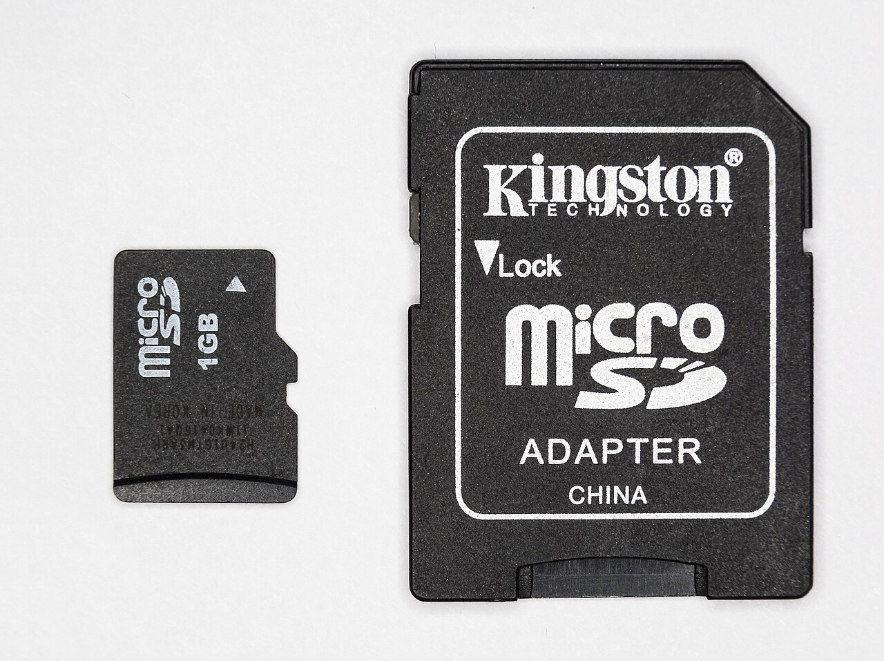A microSD memory card beside a full-sized SD adapter.