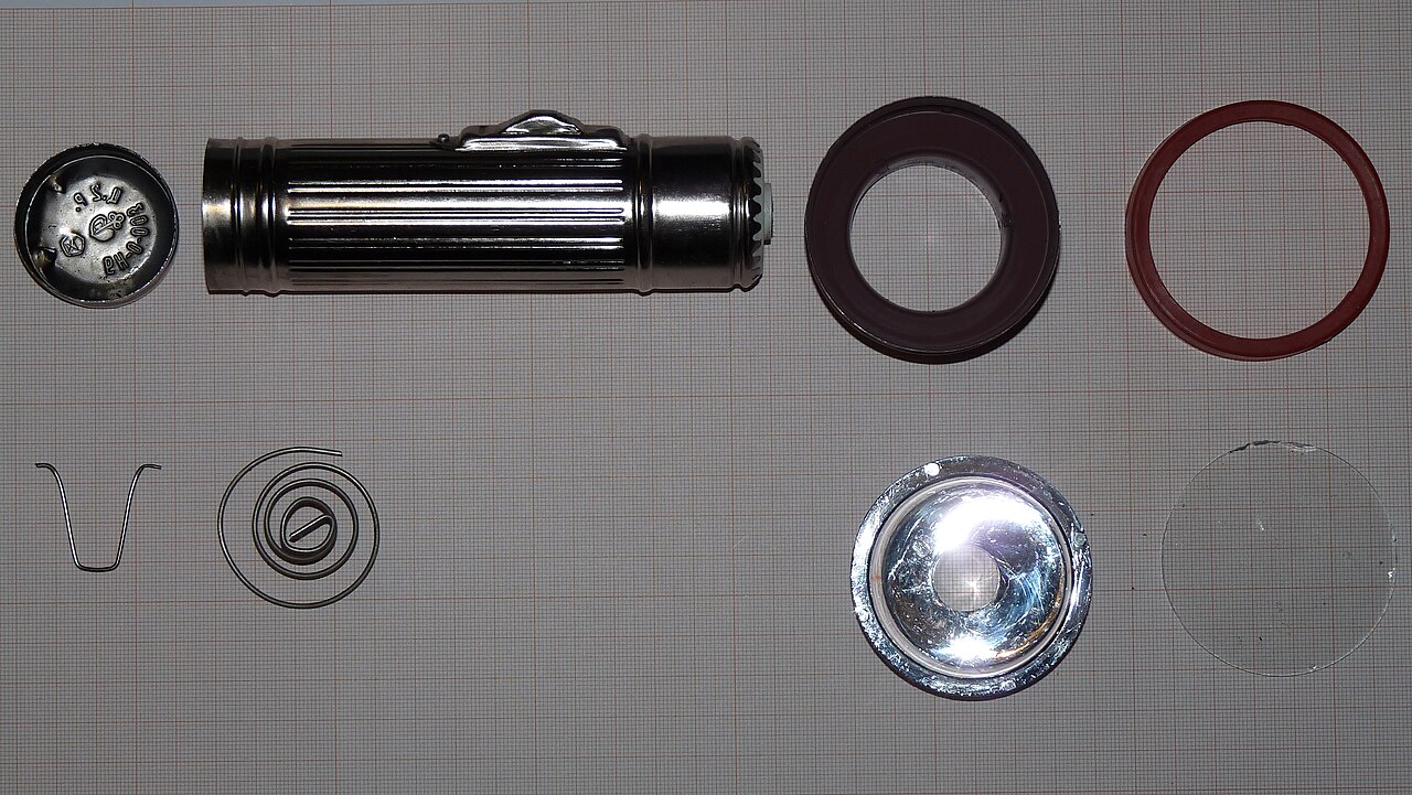 A flashlight taken apart into its case, lens, reflector and smaller components.
