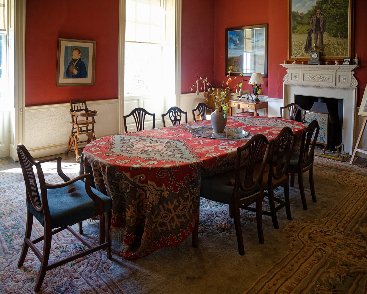 A cloth-covered dining table and wooden chairs in the red-walled dining room at Newark Park.