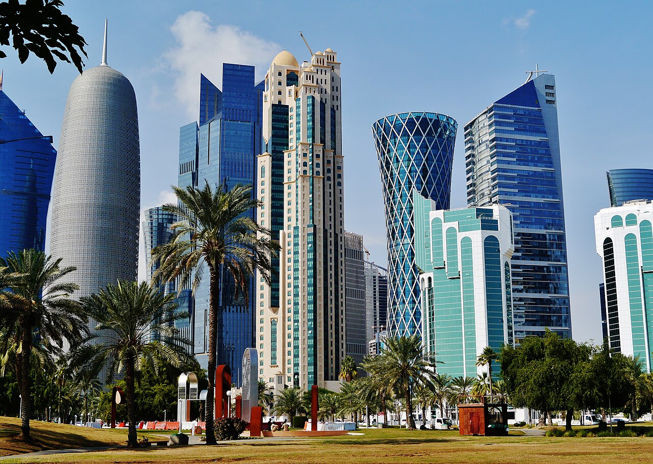 Doha towers behind a grassy park and palm trees.